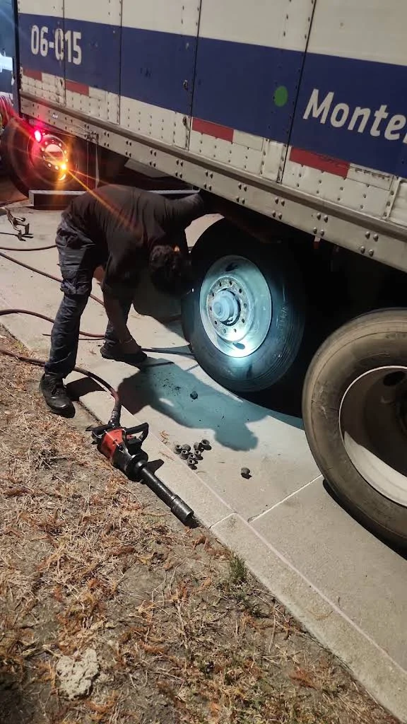 Technician beside a trailer tire during nighttime service